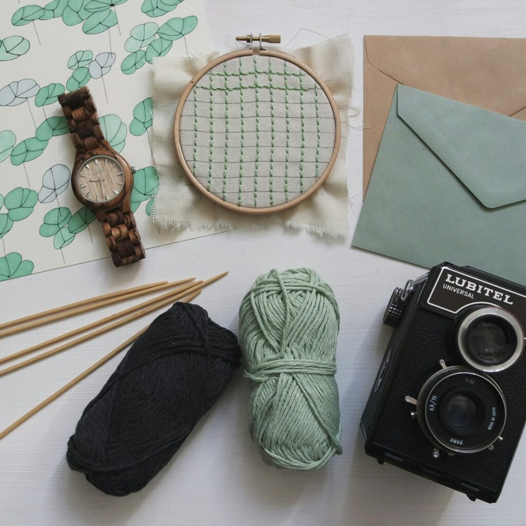 Eine Armbanduhr, ein Stickrahmen, grüne Wolle, Stricknadeln, Briefpapier und ein altmodischer Fotoapparat.