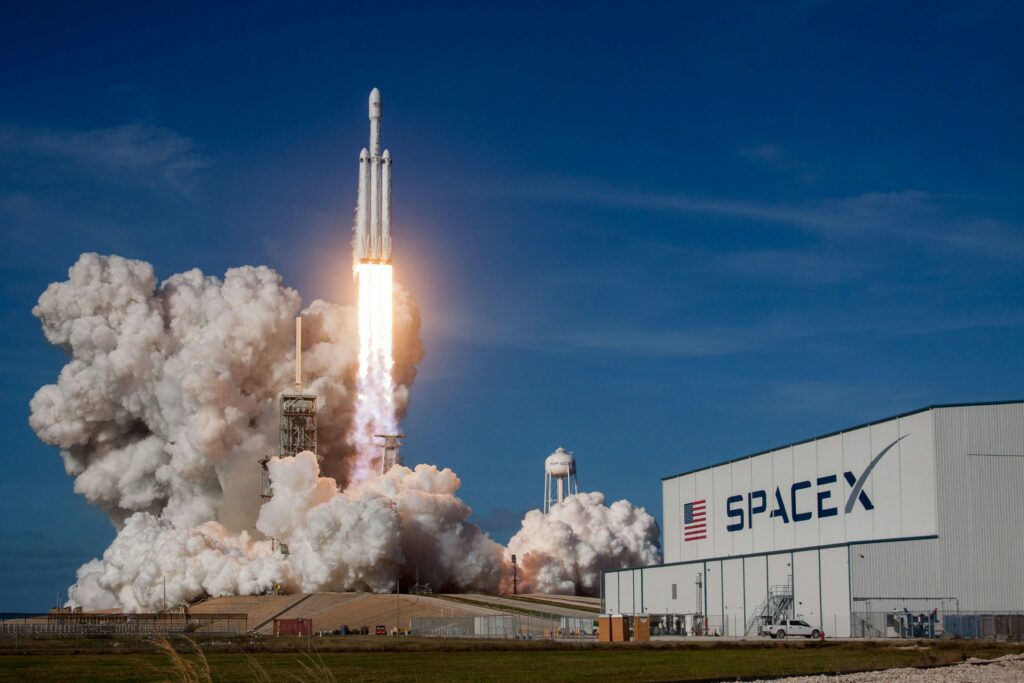 Eine Rakete startet neben einem Gebäude der Raumfahrtfirma Space X.