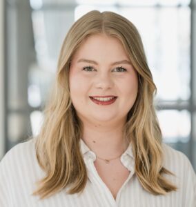 Porträt von Laura Klingelhöfer, PR-Consultant bei Adel & Link. Blondes gewelltes Haar, lächelt in die Kamera.