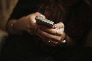 Frauenhände halten Smartphone vor unscharfem Körper, dunkler Hintergrund